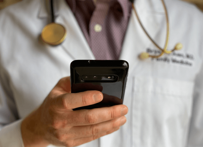 Telemedicine doctor in a white coat holding a phone doing patient care